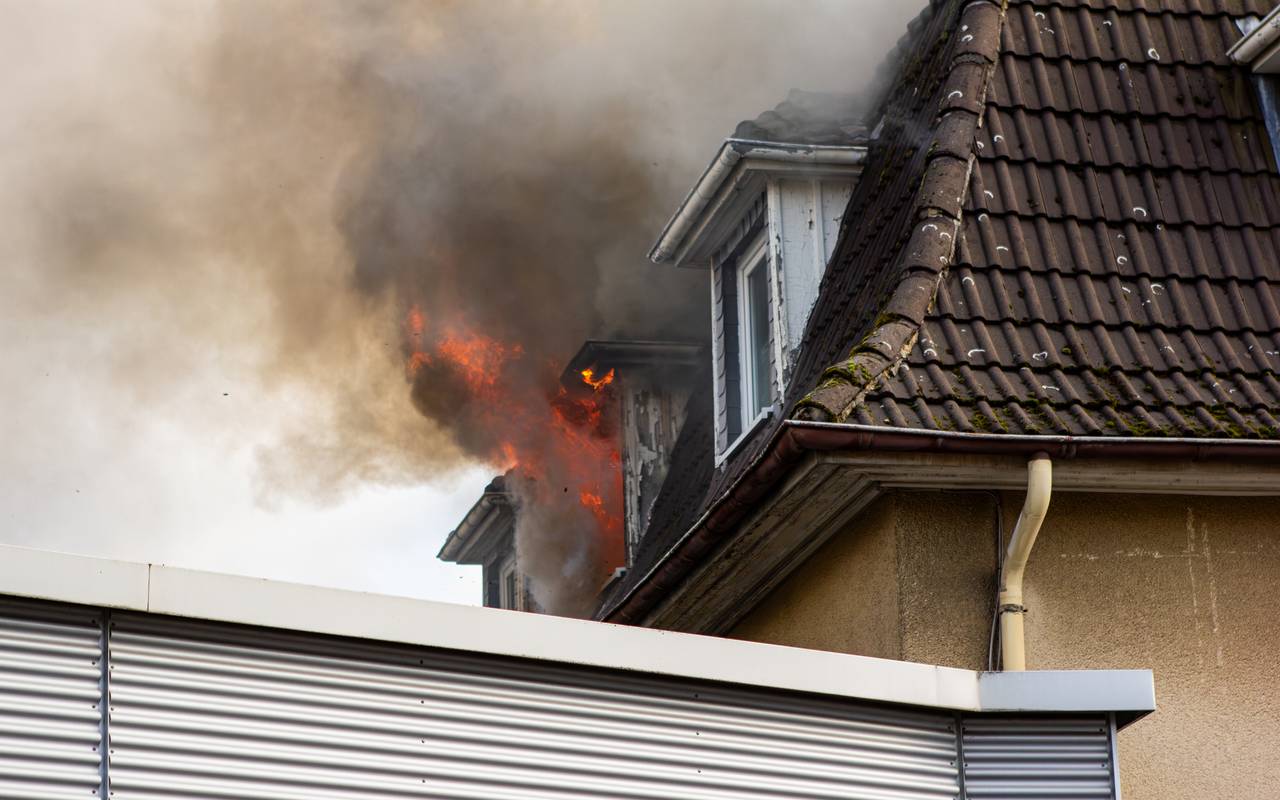 Aus einem Fenster im Dachgeschoss eines Hauses steigt schwarzer Rauch auf.