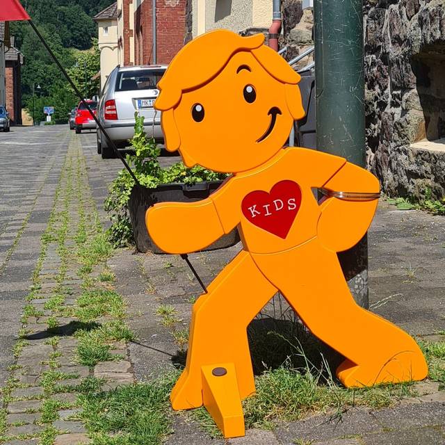 Ein orangenes Plastikmännchen steht an einem Straßenrand.