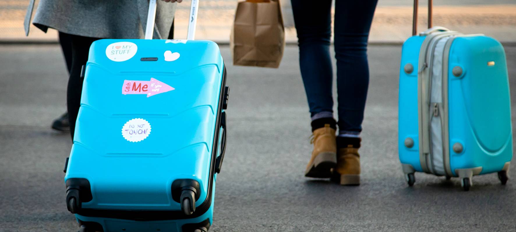 Zwei Menschen ziehen blaue Koffer hinter sich her.