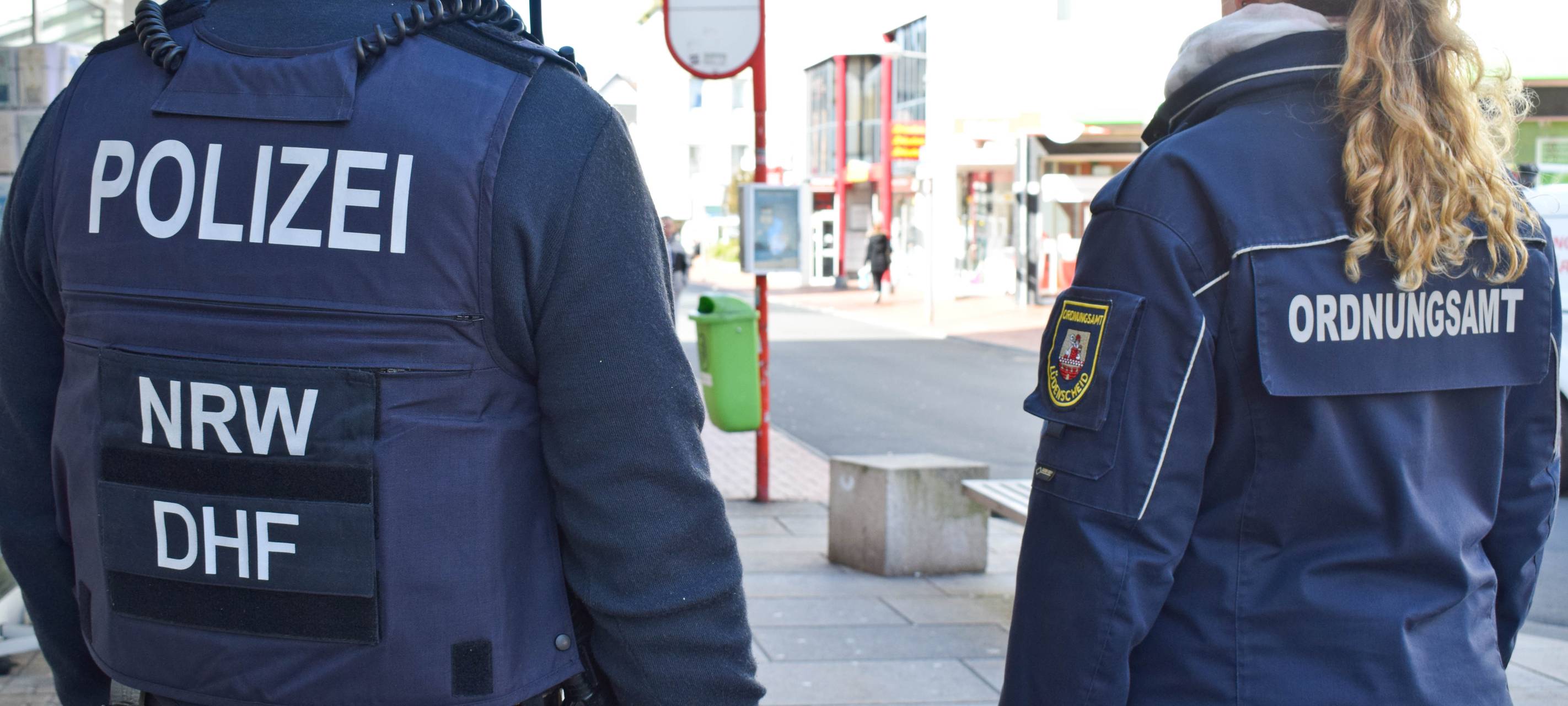 Ein Polizist und eine Polizistin stehen an einer Bushaltestelle.