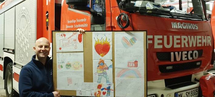 Feuerwehrmann hält großes, selbstgebasteltes Plakat in die Kamera.