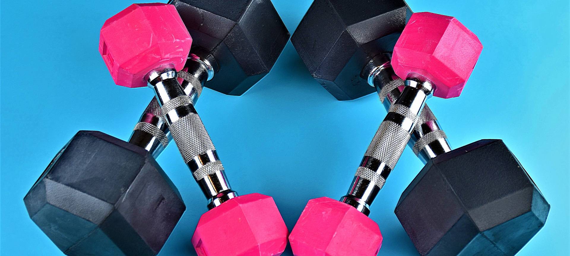 Jeweils zwei pinke und schwarze Hanteln, die gekreuzt übereinander liegen