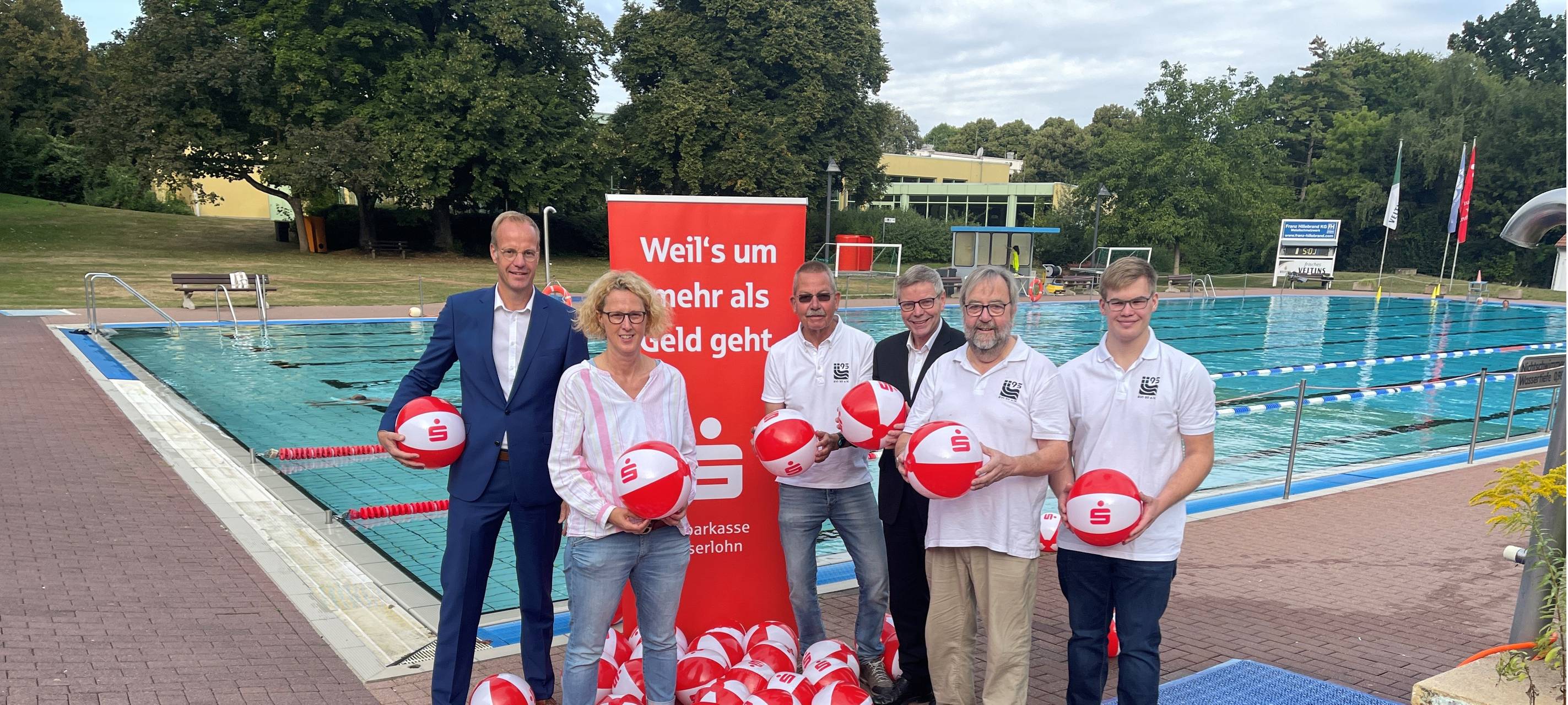 Verantwortliche von der Sparkasse und den Vereinen beim Gruppenbild vor einem Schwimmbecken im Freibad