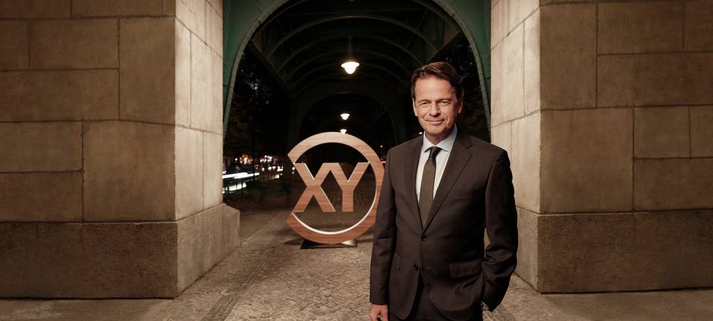 "Aktenzeichen XY... ungelöst"-Moderator Rudi Cerne in einem Anzug unter einem Torbogen vor dem Sendungslogo