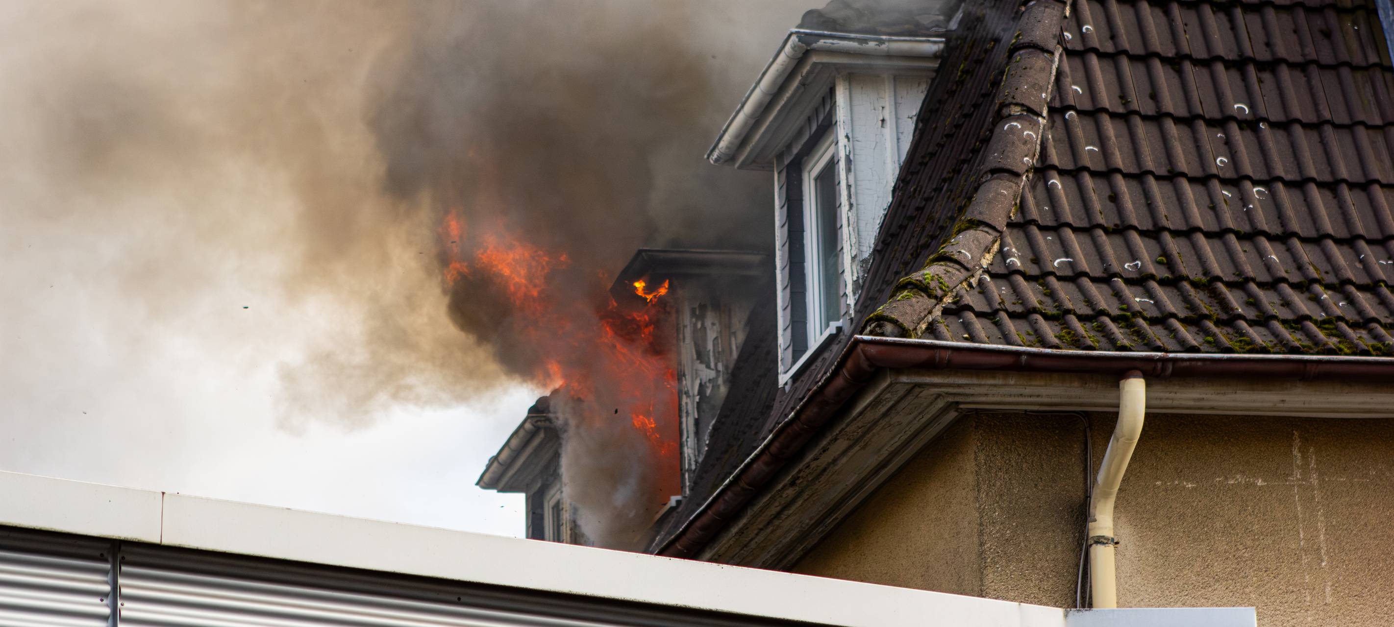 Aus einem Fenster im Dachgeschoss eines Hauses steigt schwarzer Rauch auf.