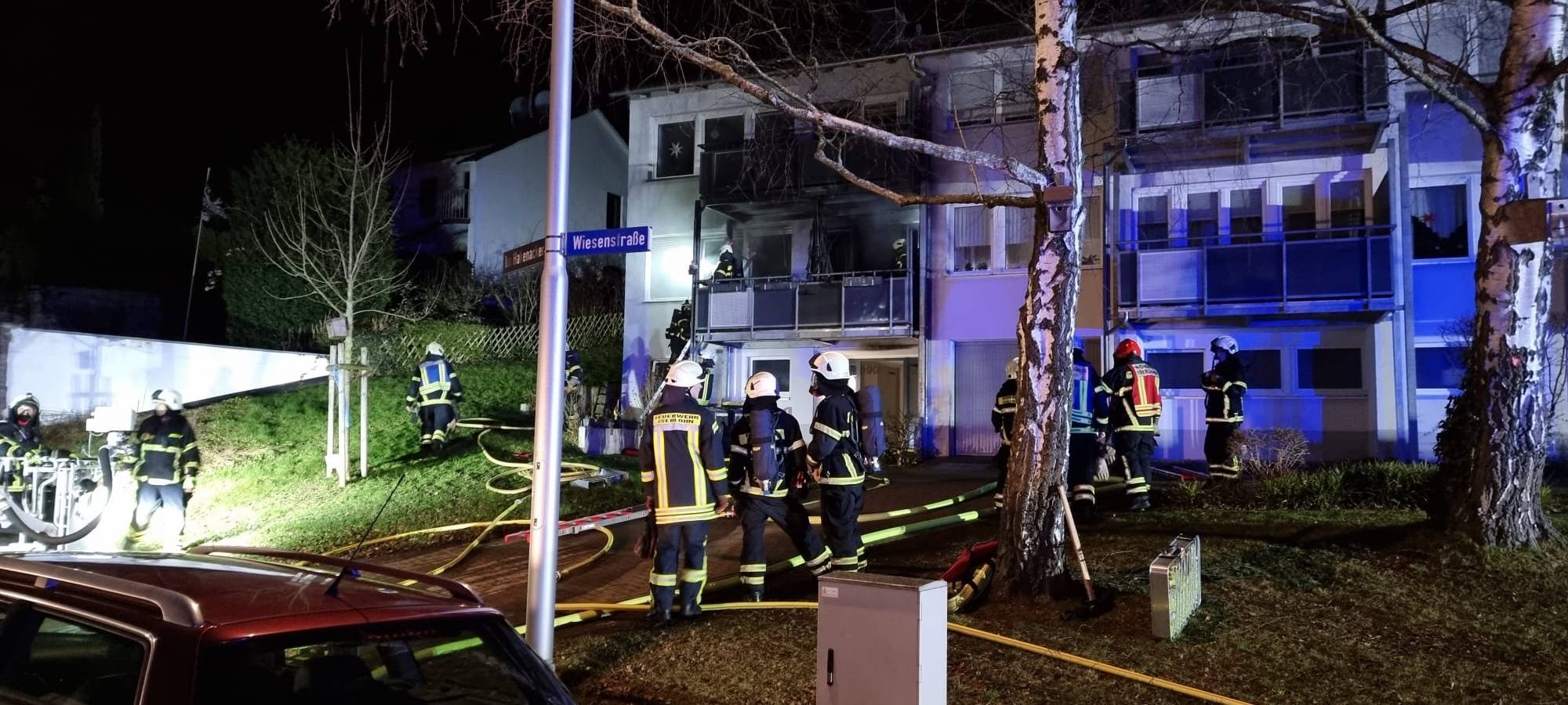 Das Bild zeigt wie Feuerwehrkräfte eine Wohnung im ersten Obergeschoss eines Mehrfamilienhauses löschen.