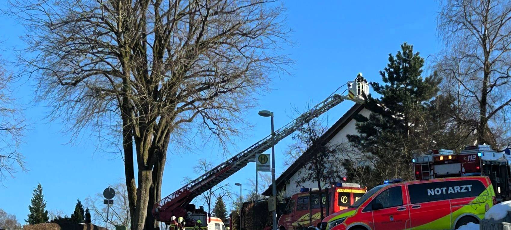 Man sieht eine Drehleiter der Feuerwehr, auf der ein Feuerwehrmann steht und den Brand eines Daches eines Wohnhauses löscht.