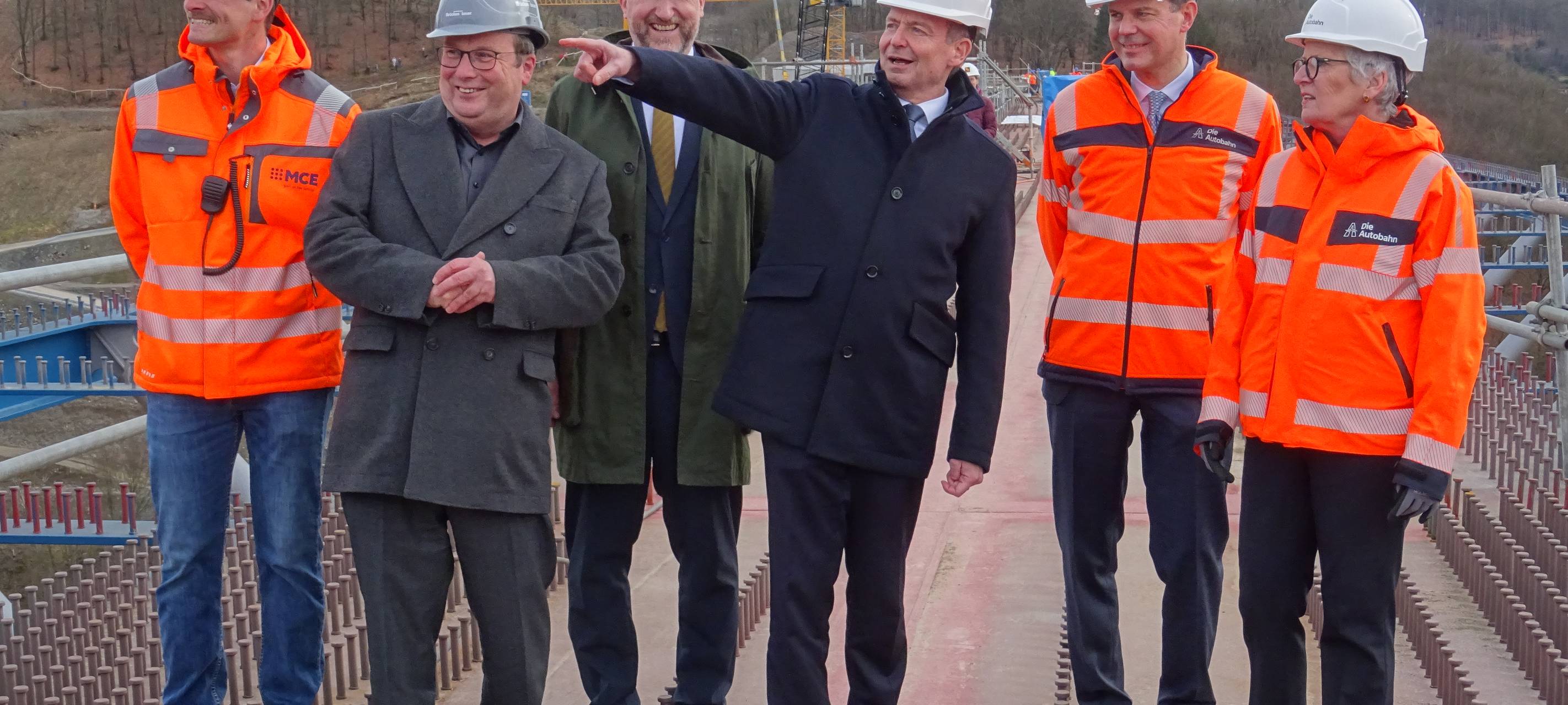 Mehrere Personen mit Bauhelmen stehen in der Nähe einer Brücke und schauen auf