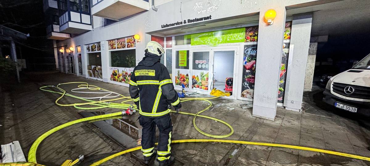 Ein Feuerwehrmann steht mit gelben Löschschläuchen vor einem Ladenlokal.