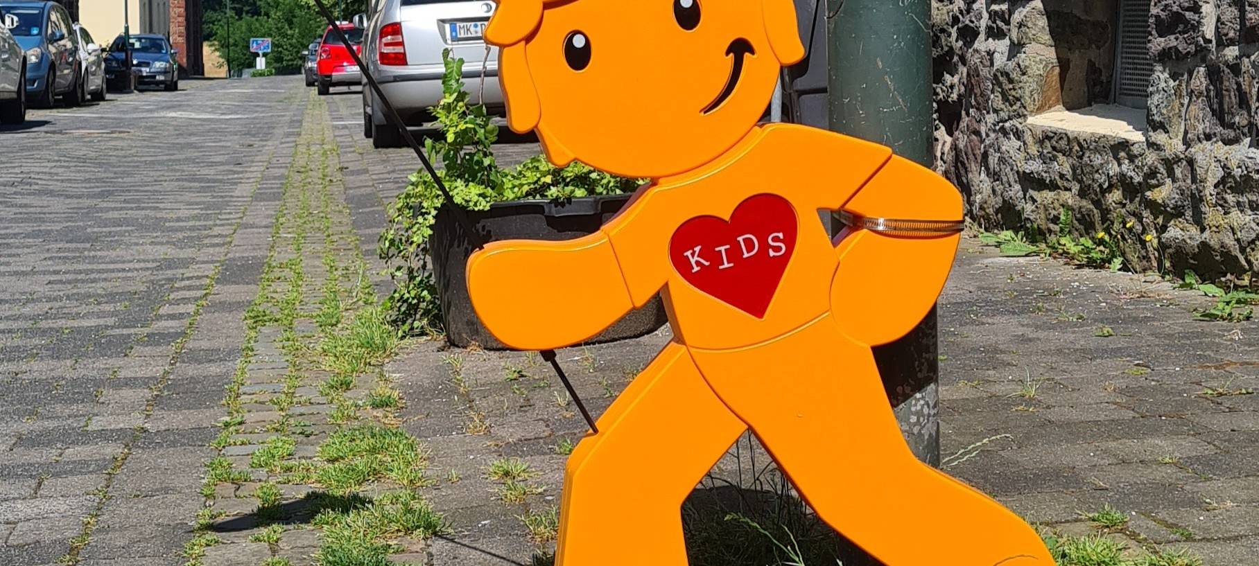 Ein orangenes Plastikmännchen steht an einem Straßenrand.