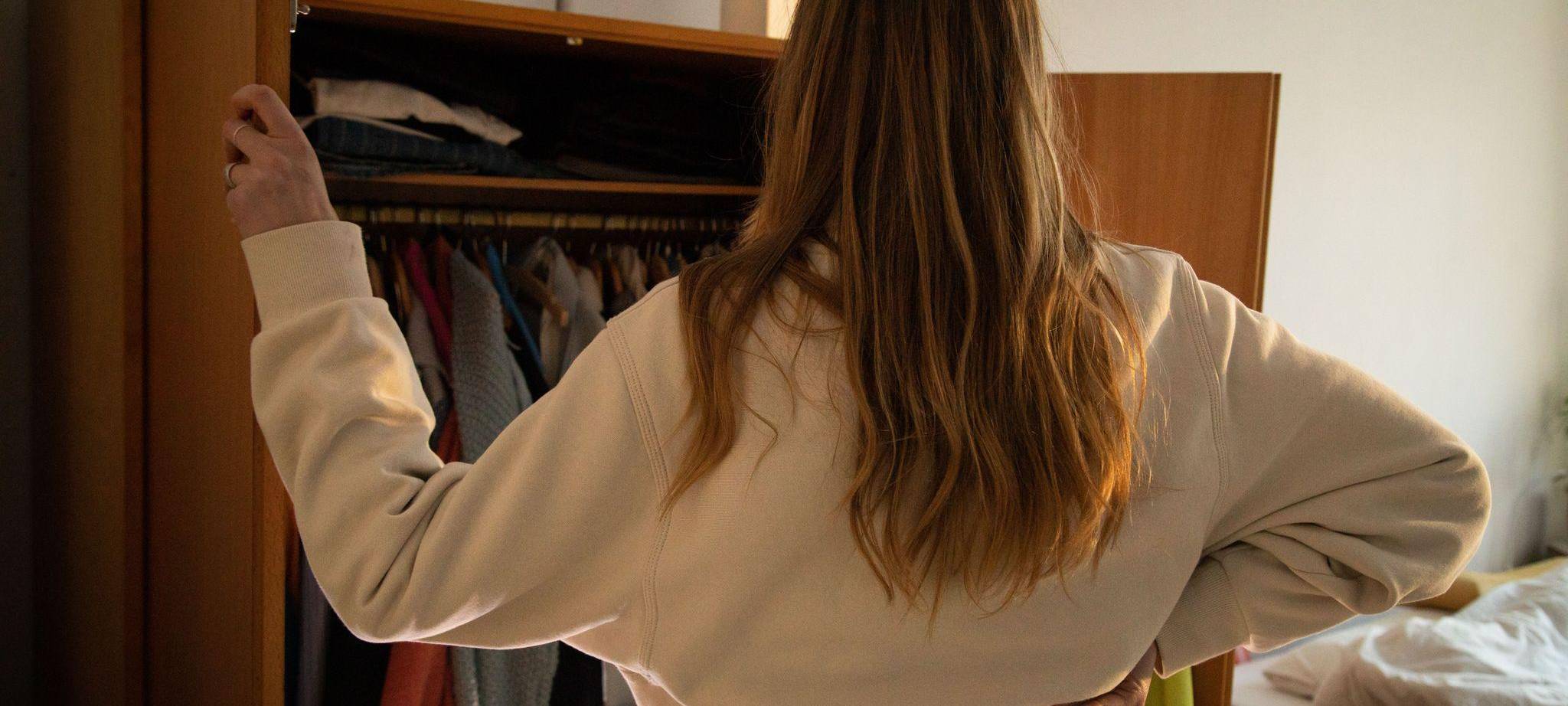 Eine Frau steht vor ihrem geoeffneten Kleiderschrank