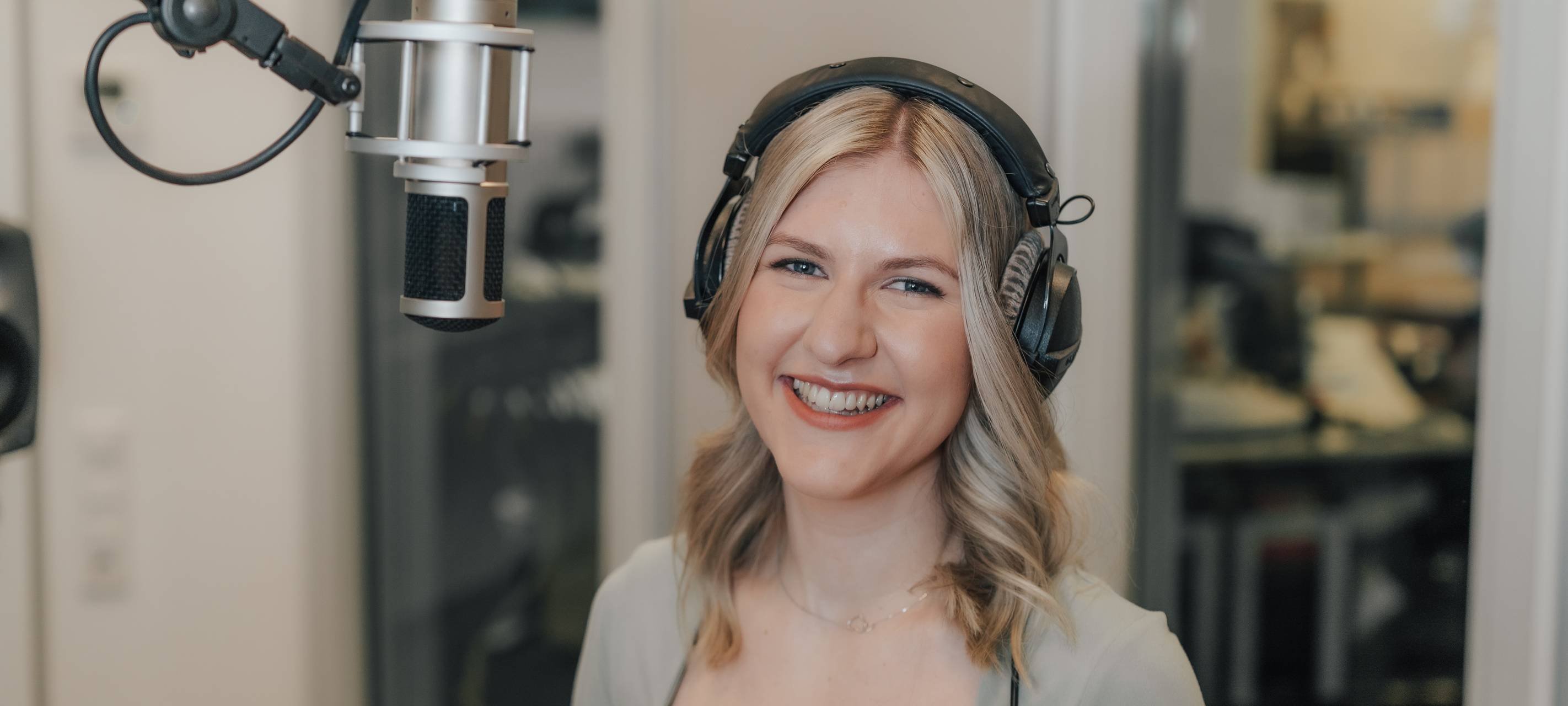 Moderatorin Pamina Klee lächelt in die Kamera. Sie steht im Radiostudio vor Mikrofon und hat die Kopfhörer auf.